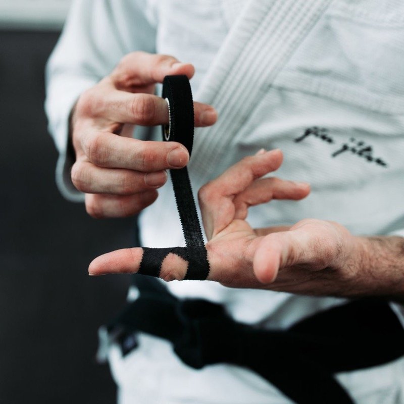 Athlete wrapping a finger with black athletic tape during a BJJ training session